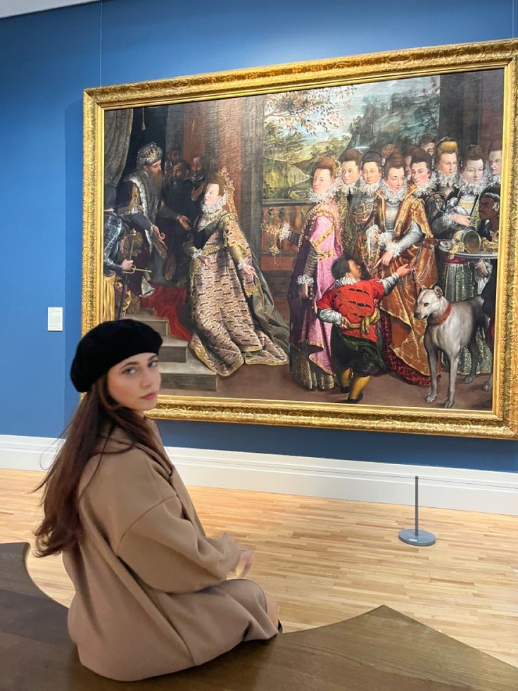 a woman sitting on the floor in front of a large painting with people dressed up