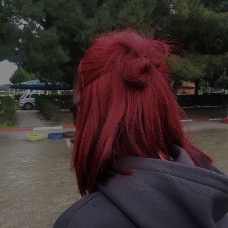 a woman with bright red hair is looking at something in the distance while wearing a gray jacket