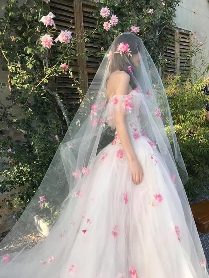 a woman in a white wedding dress with pink flowers on her veil and headpiece