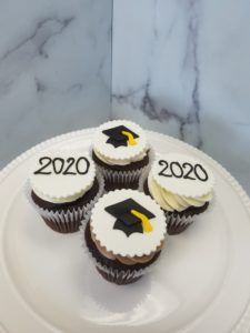 four cupcakes with graduation caps on them are sitting on a white cake plate