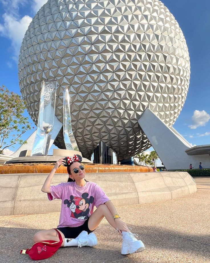 a woman sitting on the ground in front of a building with a large ball behind her