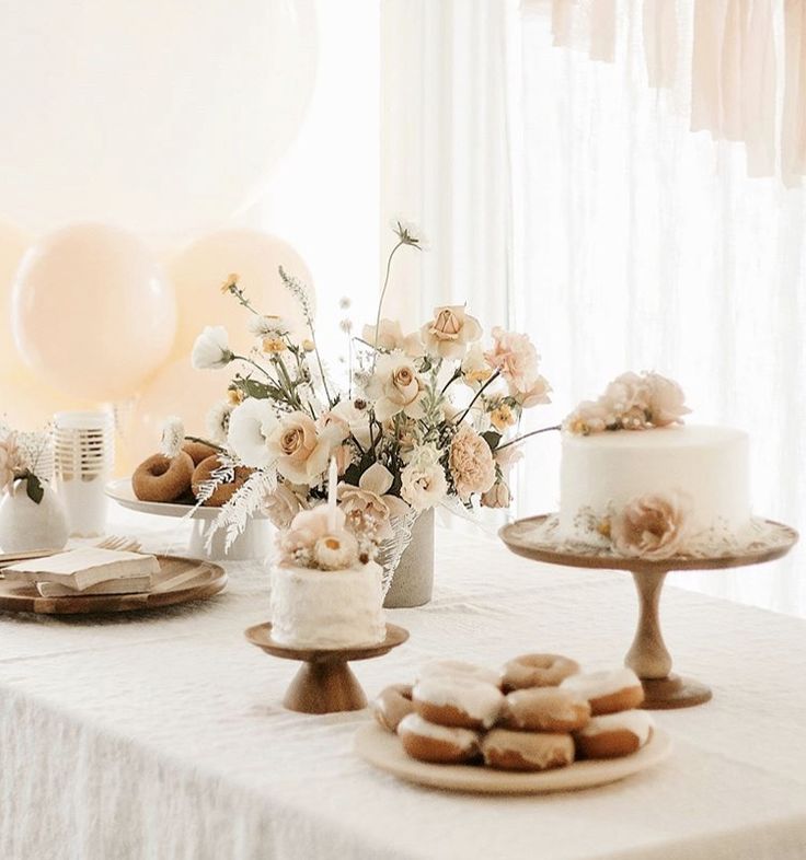 a table topped with cakes and donuts covered in frosting next to white balloons