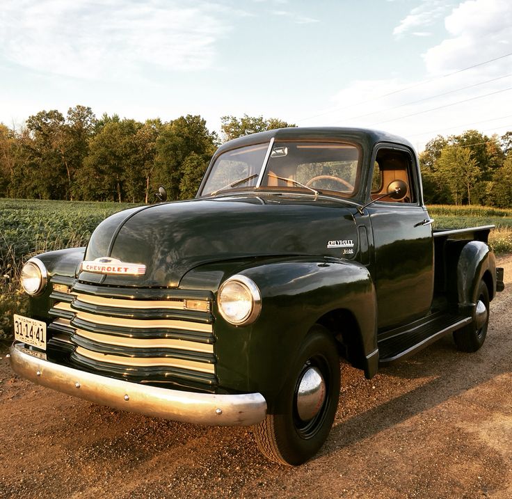 an old black truck parked in the dirt