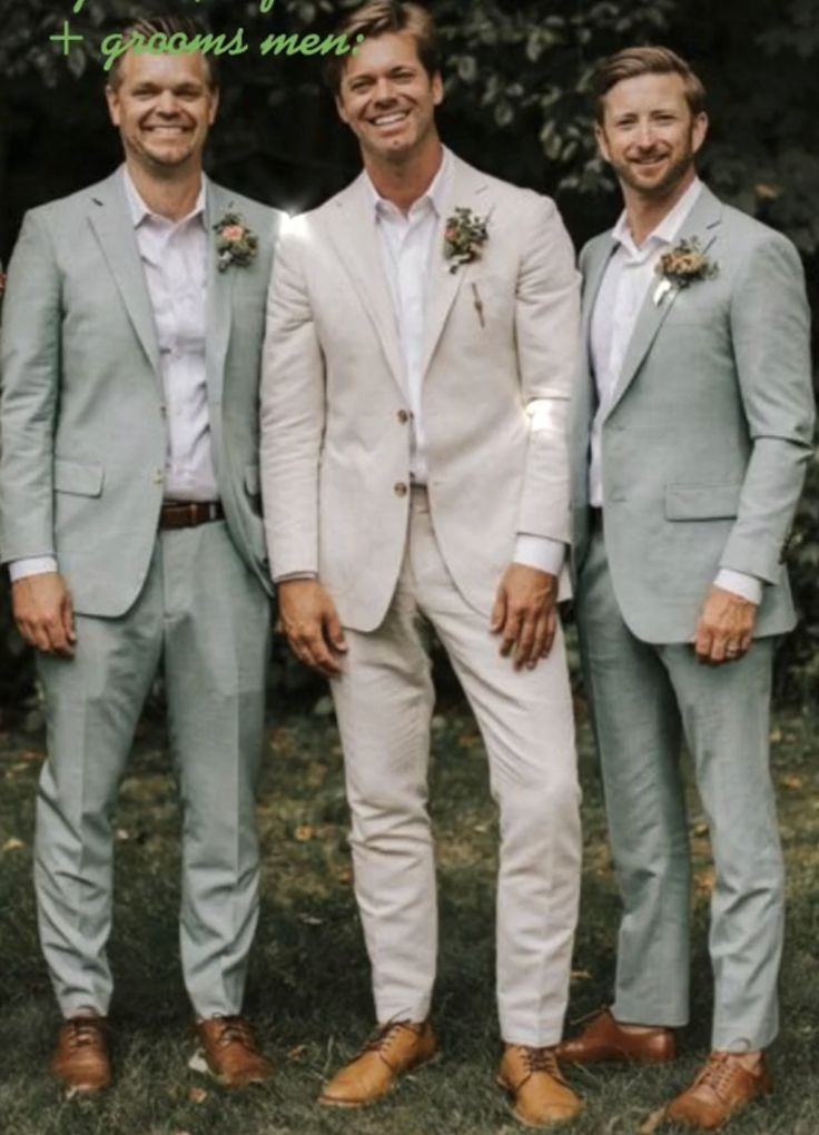 three men in suits and ties standing next to each other on the grass with trees in the background