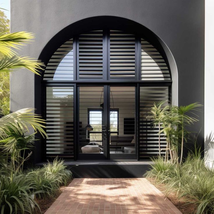 the entrance to a modern home with large arched doors and brick walkway leading into it