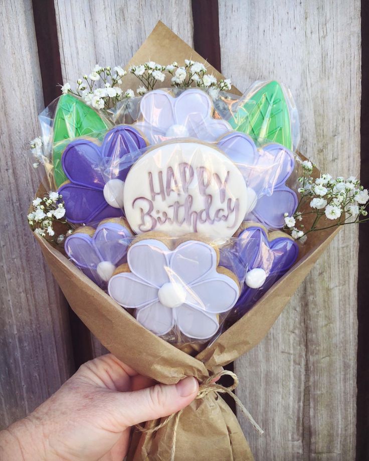 a hand holding a bouquet of cookies with the words happy birthday on it in front of a wooden fence