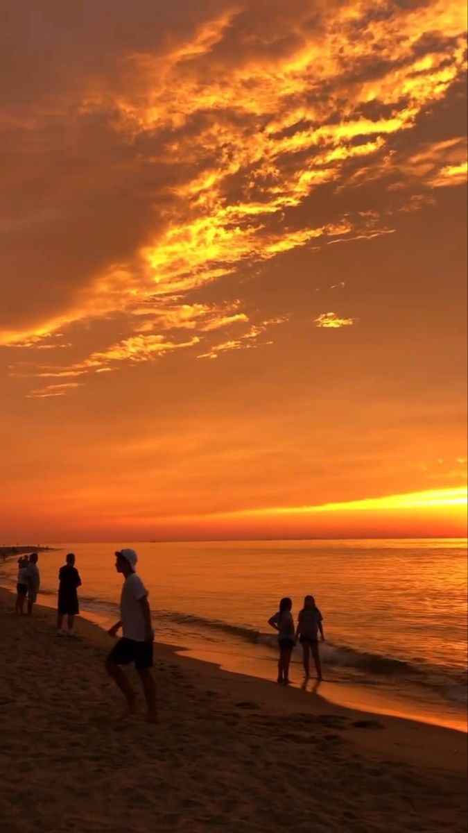 people are walking on the beach as the sun goes down in the sky over the water