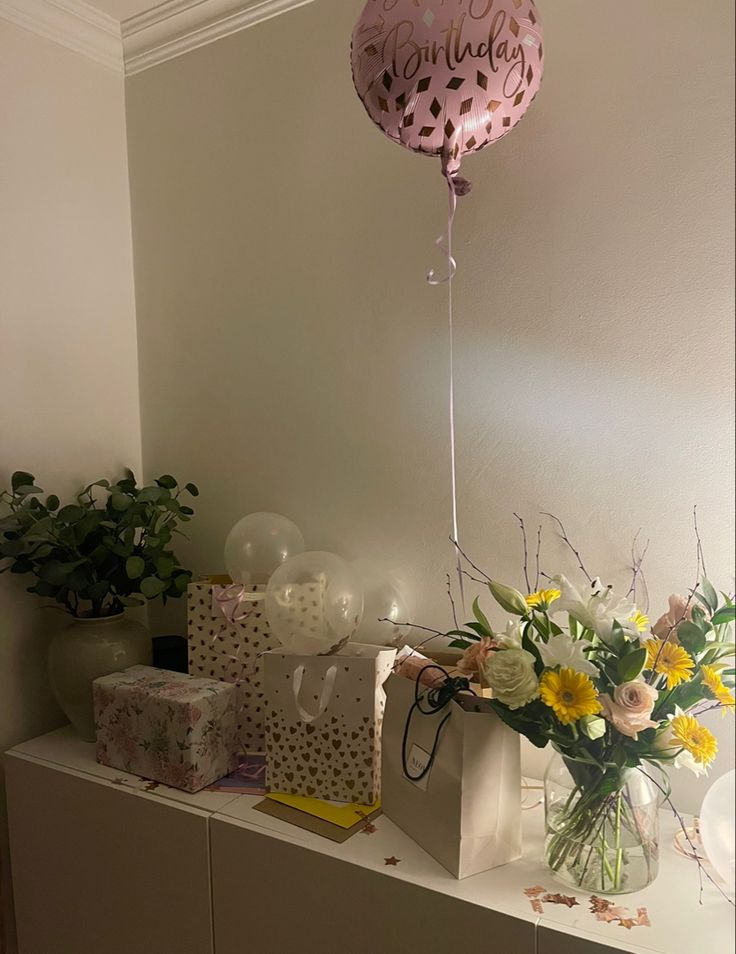 a vase filled with flowers and balloons on top of a shelf next to boxes, gift bags and other items