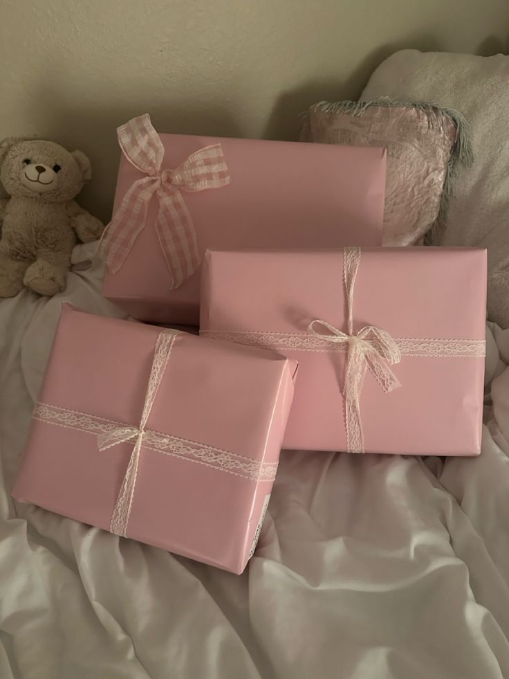 three pink wrapped presents on a bed with a teddy bear