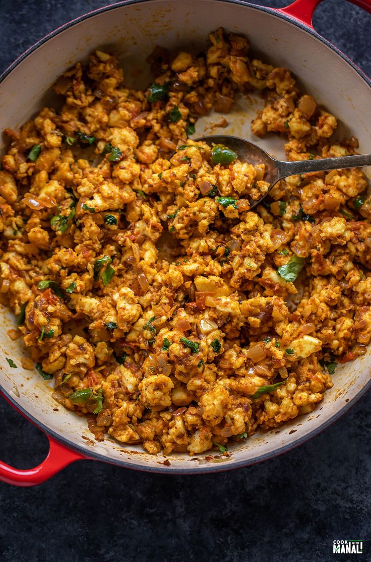 a red skillet filled with food on top of a blue countertop next to a wooden spoon