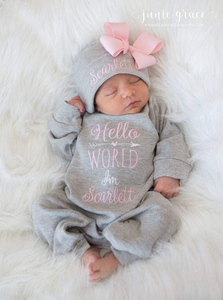 a baby girl wearing a grey onesuit with pink bows on her head and the words hello world is in spanish