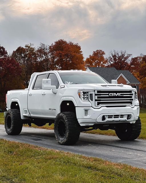 a white truck driving down a road next to a lush green field with trees in the background