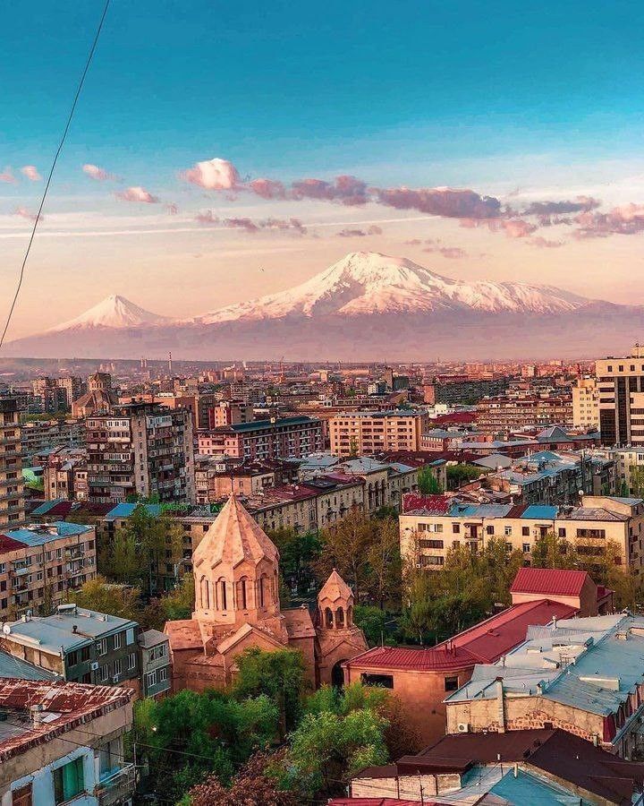 the city is surrounded by tall buildings and snow capped mountains in the distance, with an electric cable running through the foreground