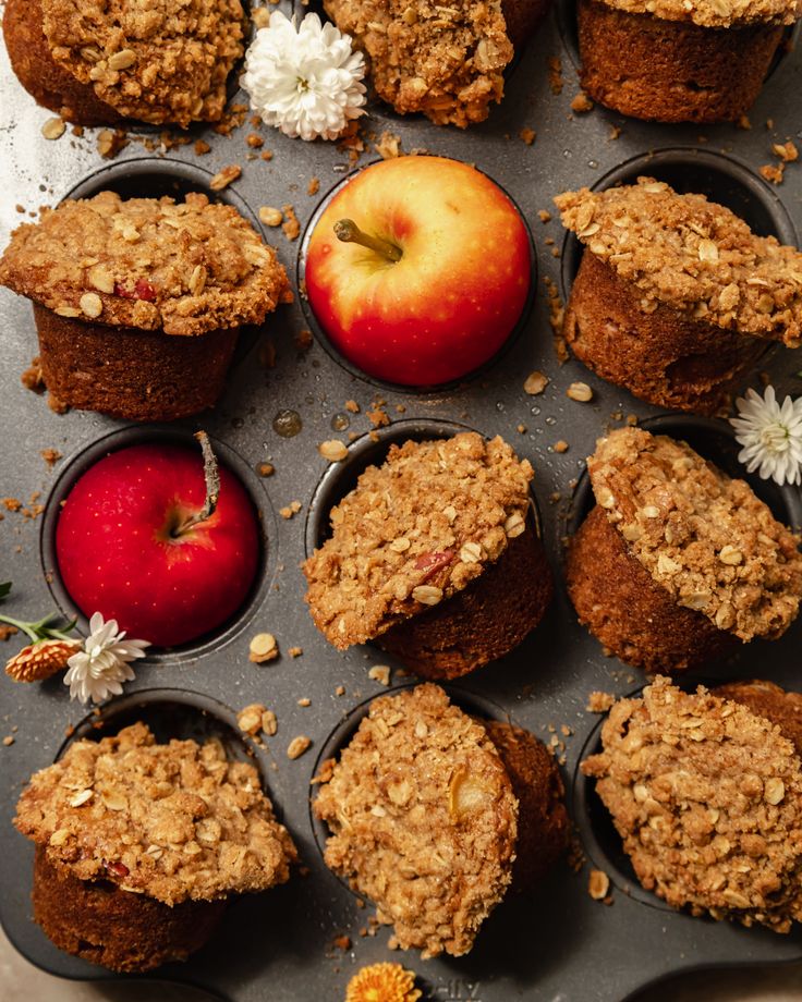 muffins and an apple on a baking tray with flowers, leaves and petals