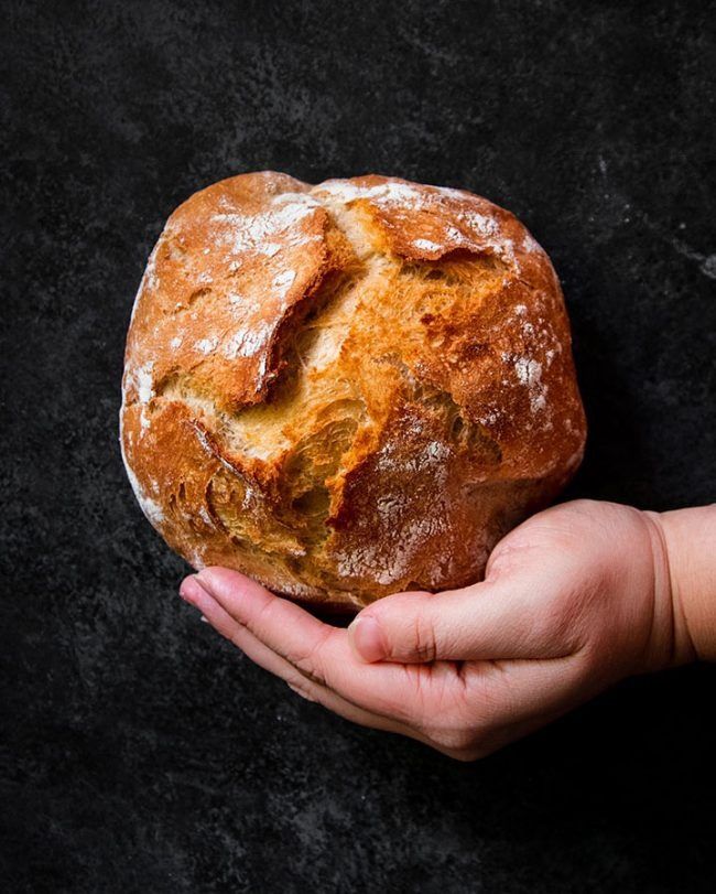 a hand holding a loaf of bread on a black surface with the top half covered in powdered sugar