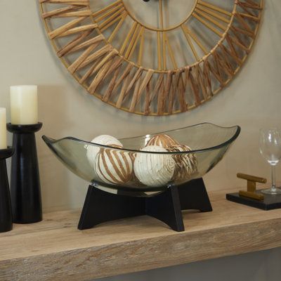 a glass bowl filled with balls on top of a wooden table next to candles and a clock