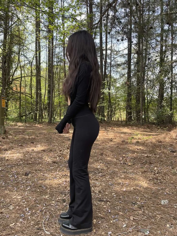 a woman standing in the woods with her back to the camera