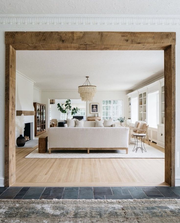 an open living room with a couch and fireplace in the corner, viewed through a large wooden frame