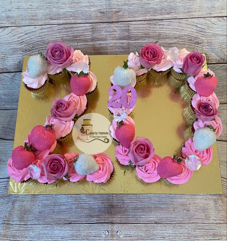 a cake shaped like the number 20 with pink flowers and white pom poms