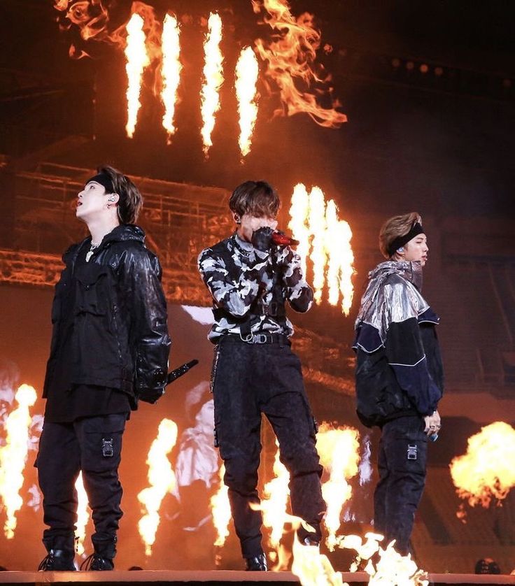 three young men standing on top of a stage with flames in the air behind them