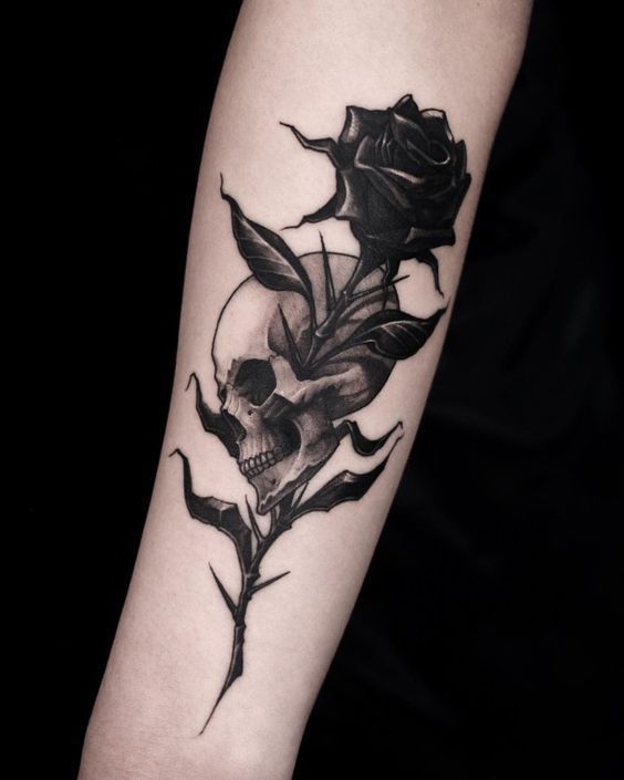 a black rose and skull tattoo on the left upper arm, with leaves coming out of it