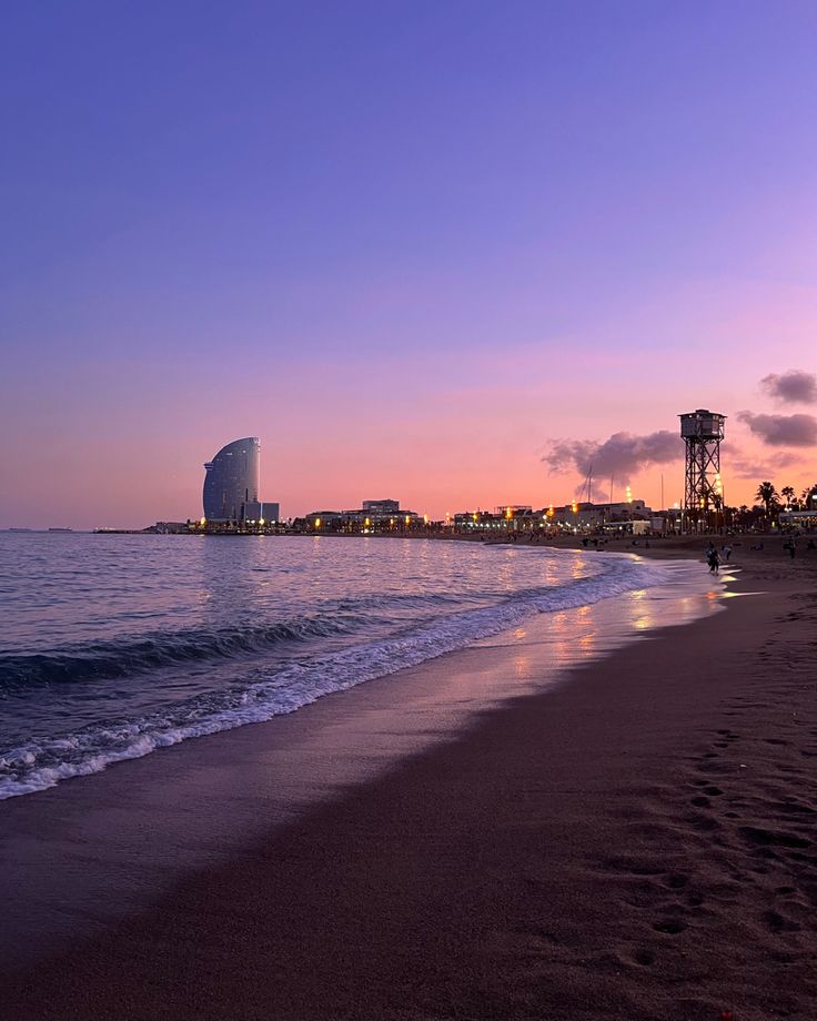 the sun is setting at the beach with buildings in the background