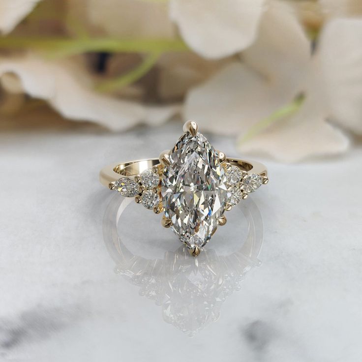 a three stone diamond ring sitting on top of a marble table next to white flowers