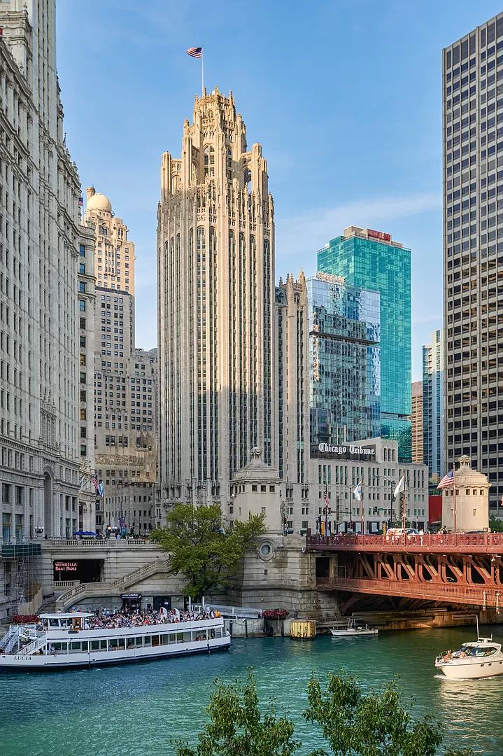 a boat is in the water near some tall buildings and a bridge with people on it