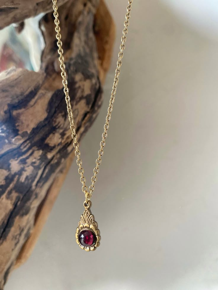 A precious handmade antique gold necklace with a unique solid vintage floral motif antique brass pendant and a high quality garnet. Garnet is the January birthstone and also the stone that celebrates the 2nd wedding anniversary symbolising love and devotion. It is deep red in colour and is known to be a gemstone that purifies and balances energy and the chakras. The chain of the necklace is gold plated of a very good quality with a fastening at the back to keep your necklace securely on at all t Antique Garnet Pendant Necklace, Brass Locket Necklace With Flower Pendant, Brass Flower Pendant Locket Necklace, Vintage Ruby Gemstone Necklaces, Antique Gold Necklaces With Vintage Charm And Oval Pendant, Antique Gold Necklace With Oval Pendant And Vintage Charm, Antique Gold Oval Pendant Necklace With Vintage Charm, Antique Gold Necklace With Vintage Charm Oval Pendant, Ornate Oval Pendant Necklace With Vintage Charm