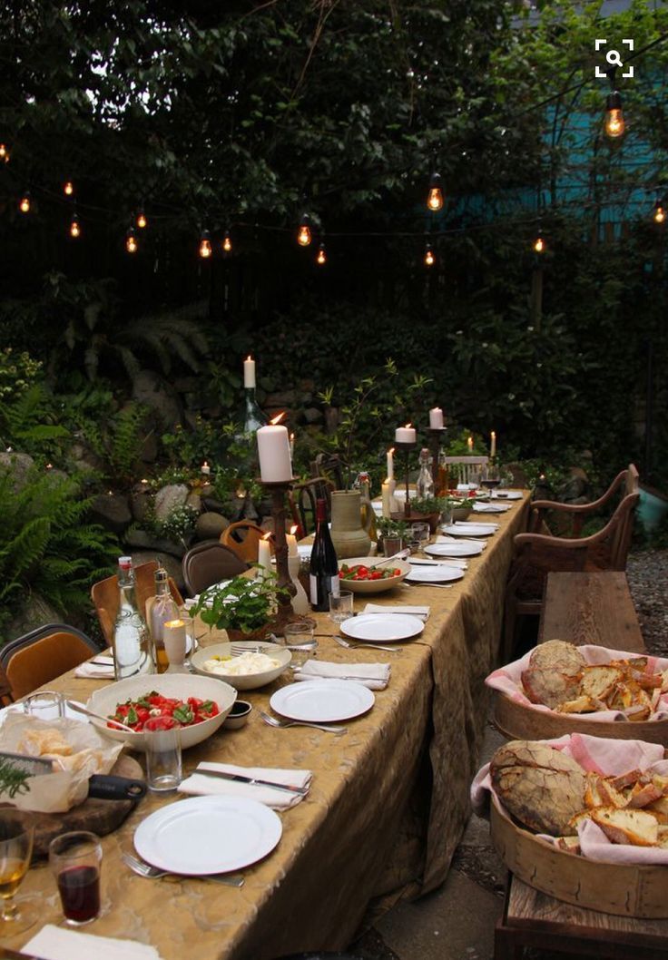 a long table is set up with plates and food for an outdoor dinner in the woods