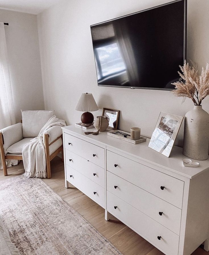 a flat screen tv mounted on the wall above a white dresser in a living room