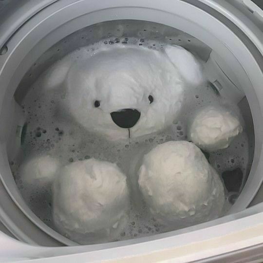 a white teddy bear sitting in a washing machine filled with foamy bubbles and water