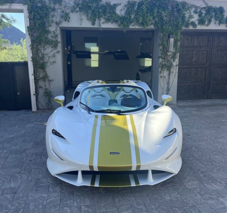 a white and yellow sports car parked in front of a garage with an open door