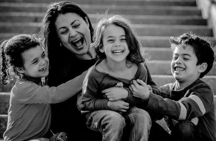 a woman and three children sitting on steps with their arms around each other, laughing