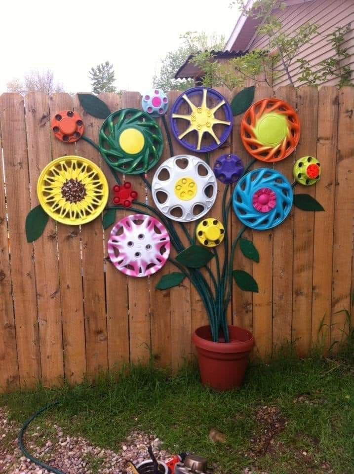 a tree made out of paper plates sitting on top of a grass covered yard next to a fence