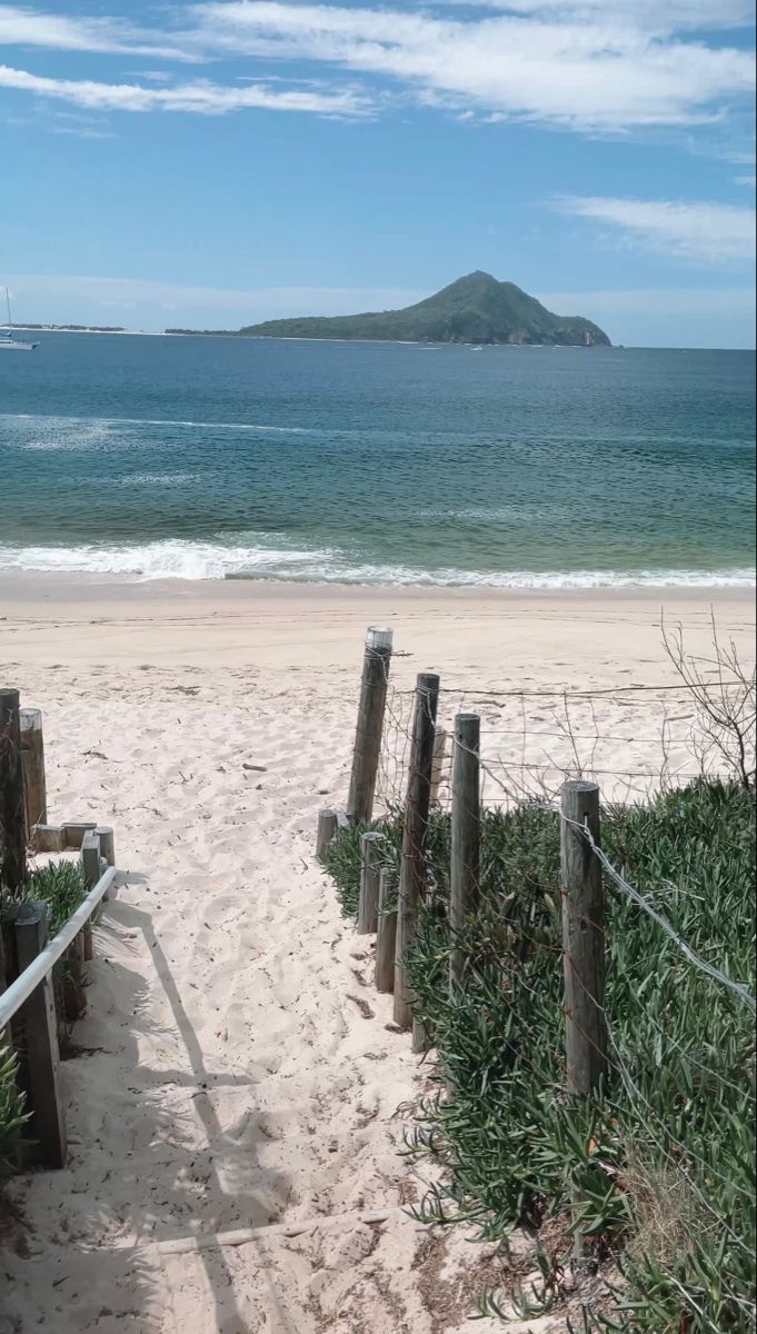 a wooden fence on the beach leading to an ocean and sand area with mountains in the distance