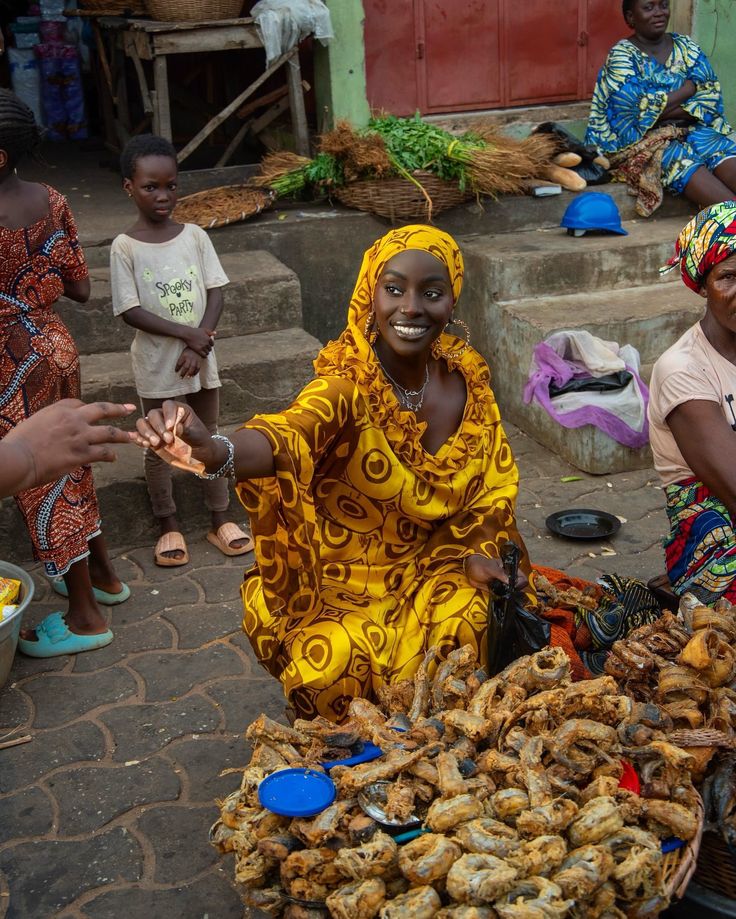 a woman sitting on the ground in front of some baskets filled with food and people standing around