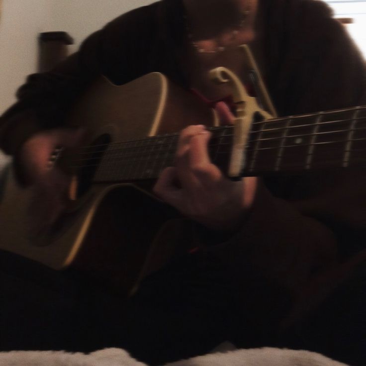 a man sitting on top of a bed playing a guitar