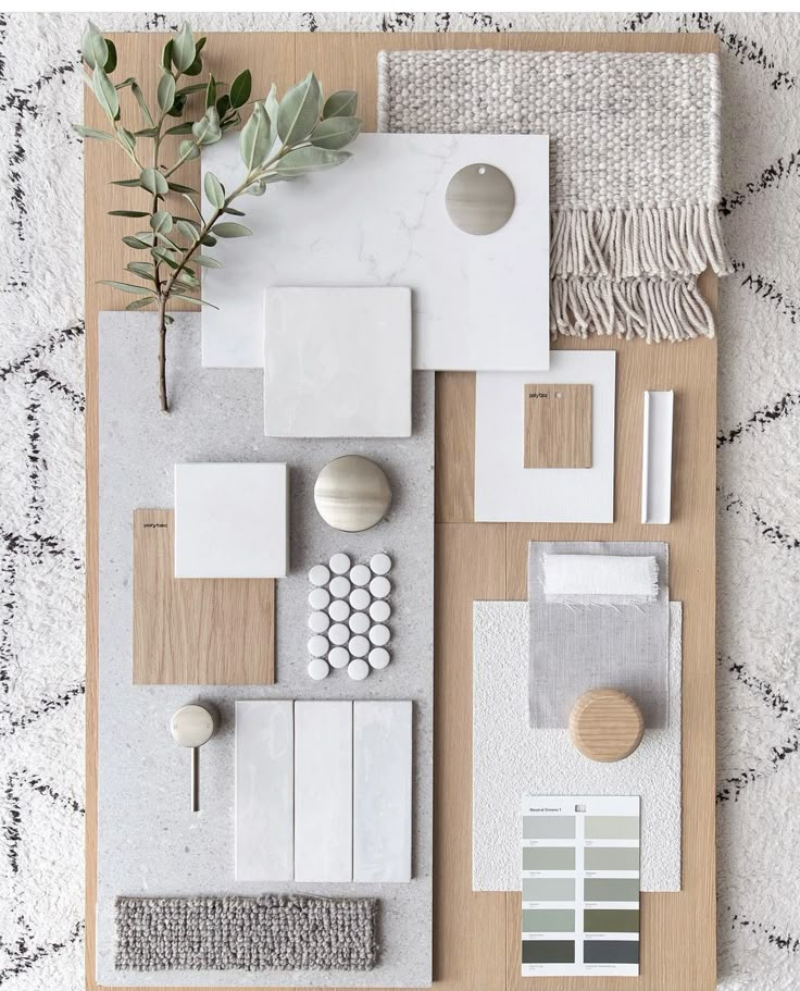 an arrangement of white and grey items on a wooden tray with greenery in the middle