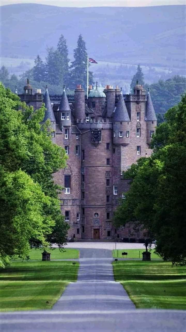 an old castle is surrounded by trees in the middle of a road that leads to it