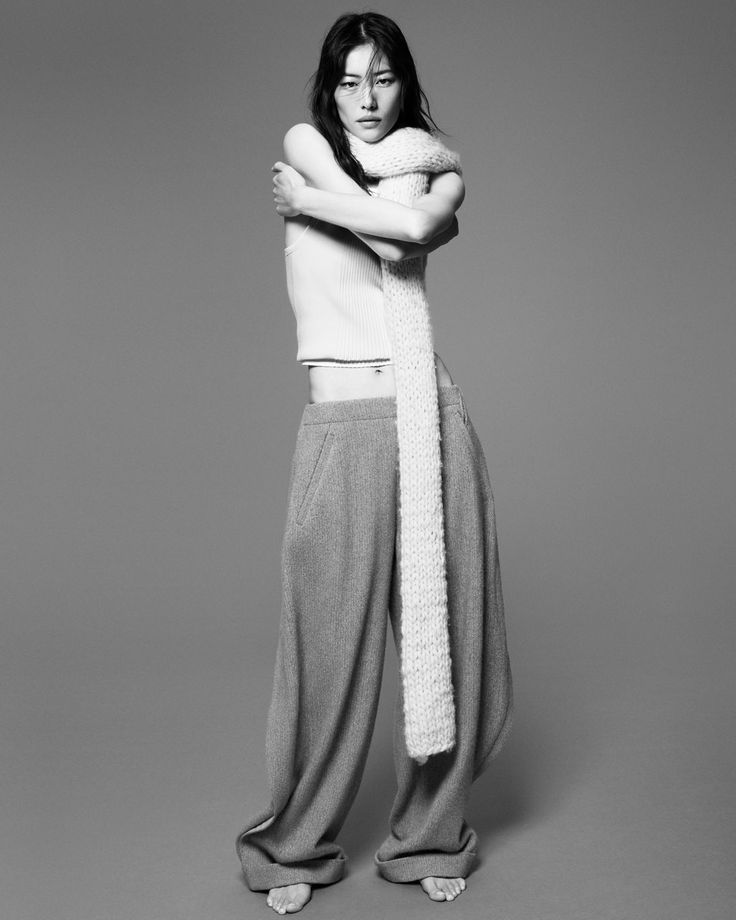 a woman is standing with her arms crossed and looking at the camera while wearing wide pants