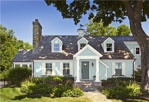 a blue house with white trim on the front door and windows is surrounded by greenery