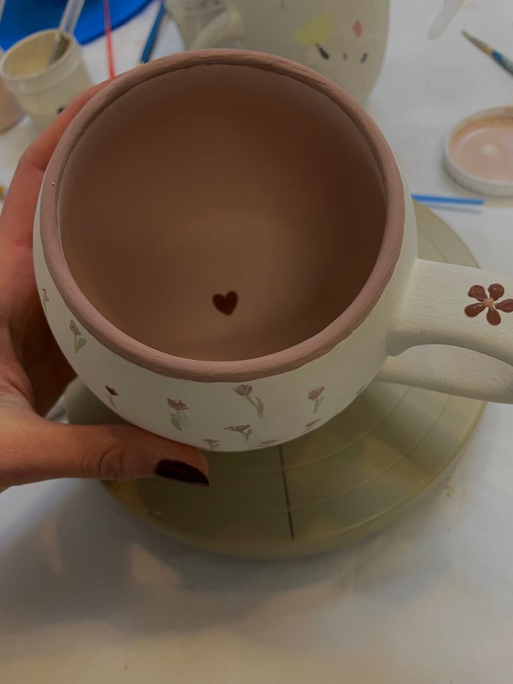 a hand holding a coffee cup on top of a saucer with hearts painted on it