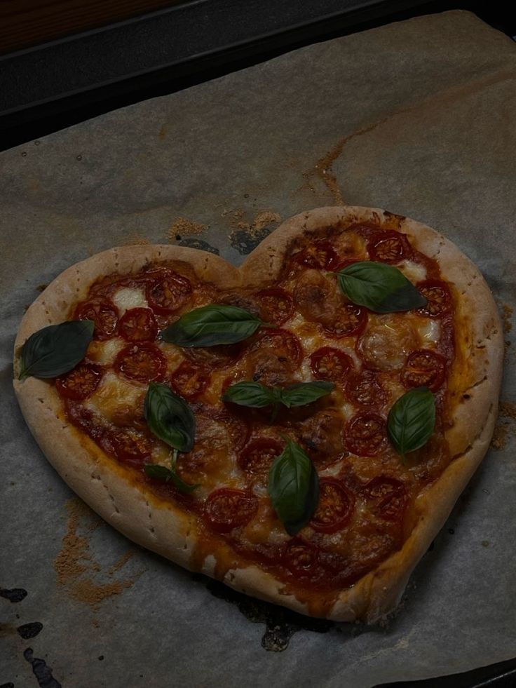 a heart shaped pizza sitting on top of a piece of wax paper with basil leaves