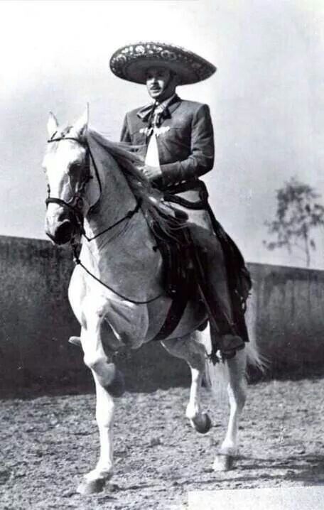 a man riding on the back of a white horse wearing a sombrero over his head