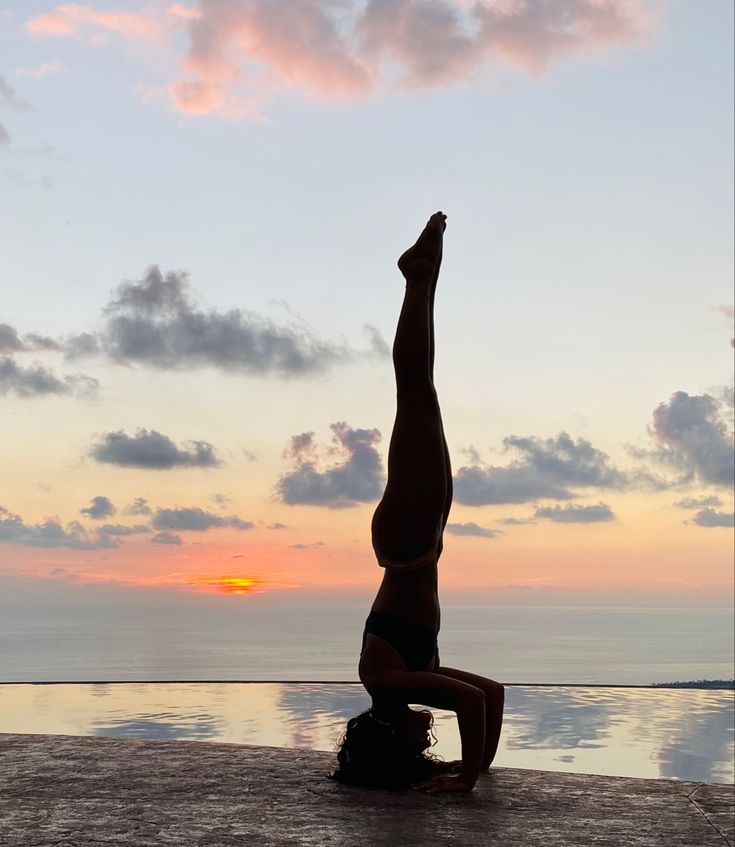 a person doing a handstand in front of a body of water at sunset