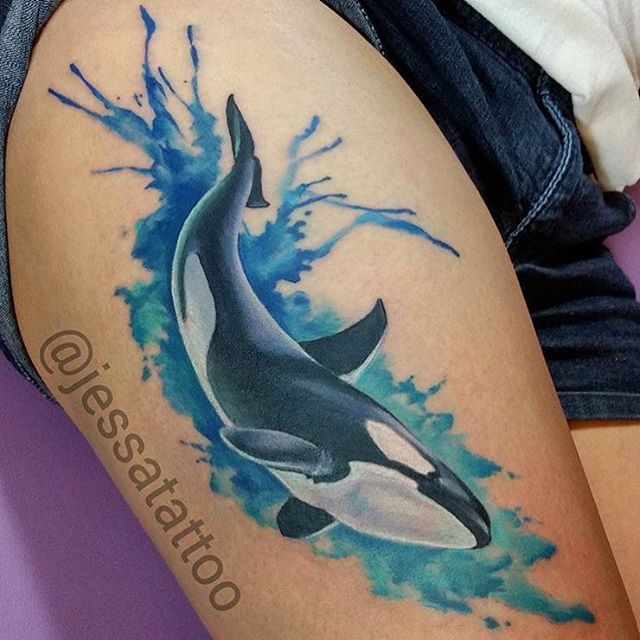 an orca killer whale tattoo on the thigh with blue water splashing around it