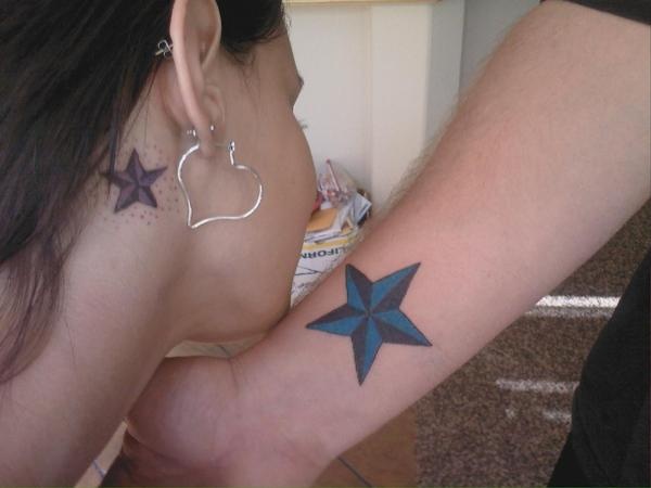 a woman with a blue star tattoo on her left arm and behind her ear, looking down at the ground