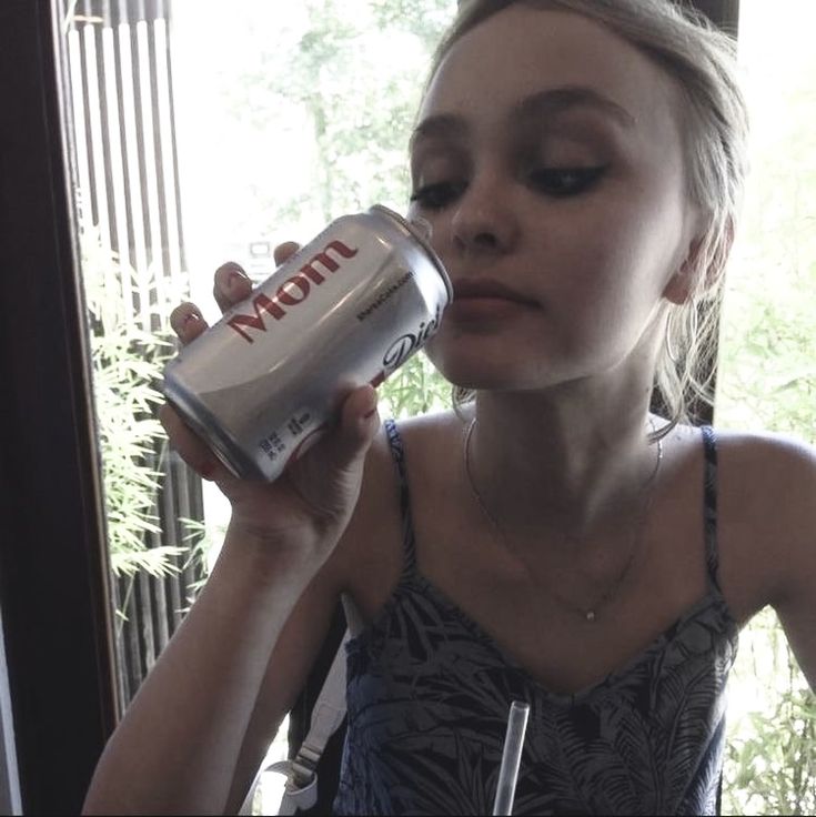 a woman drinking from a can in front of a window