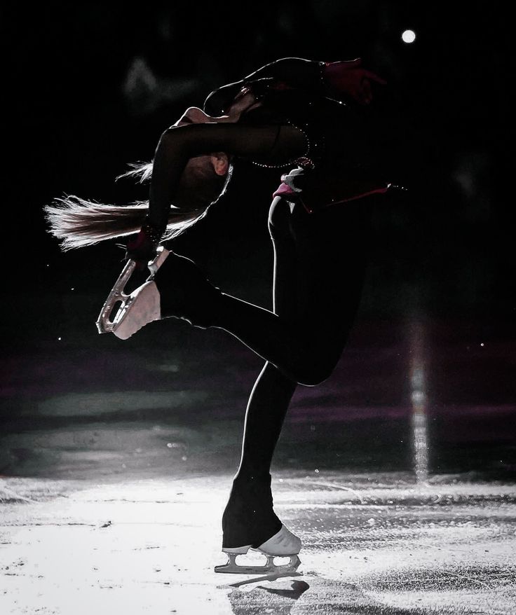 a female figure skating on an ice rink in the dark with her legs spread out